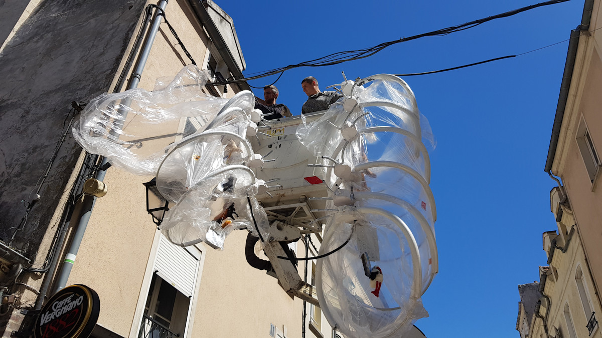 Christophe Alzetto prépare l'installation Cadavre Exquis, à l'aide des ouvriers de la ville et d'une nacelle. On voit l'accrochage en hauteur et ses difficultés