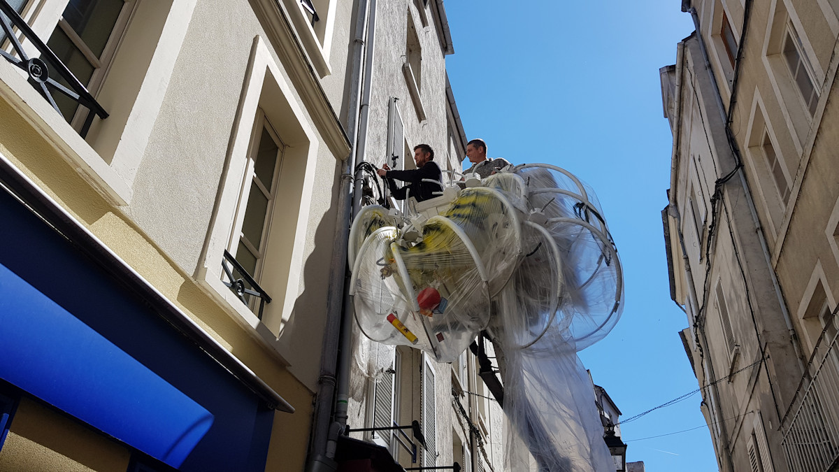 Christophe Alzetto prépare l'installation Cadavre Exquis, à l'aide des ouvriers de la ville et d'une nacelle. On voit l'accrochage en hauteur et ses difficultés